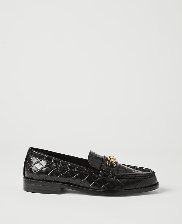A black, crocodile-embossed loafer with a gold buckle sits on a plain white background.