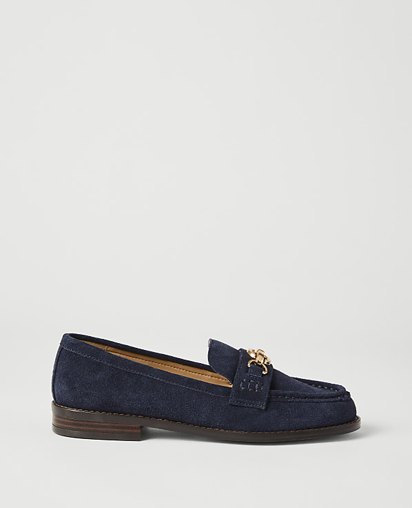 A navy blue suede loafer with a gold buckle sits on a plain white background.