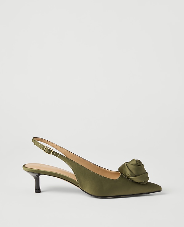 A green satin slingback heel with a rose embellishment rests on a plain white background.