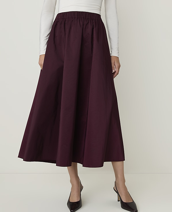 A person in a burgundy skirt and white top stands against a plain white background.