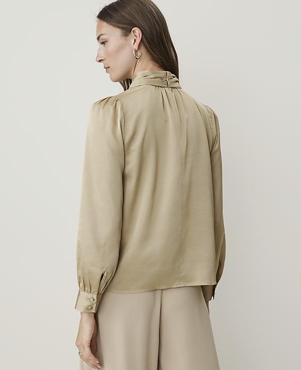 A woman in a satin blouse and skirt stands against a plain, light background.