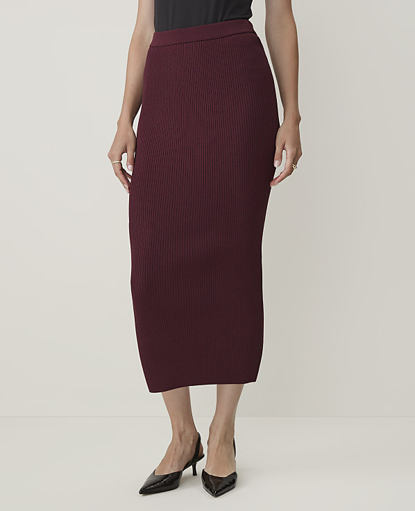 A person stands in a ribbed burgundy midi skirt and black slingback heels against a plain, light background.