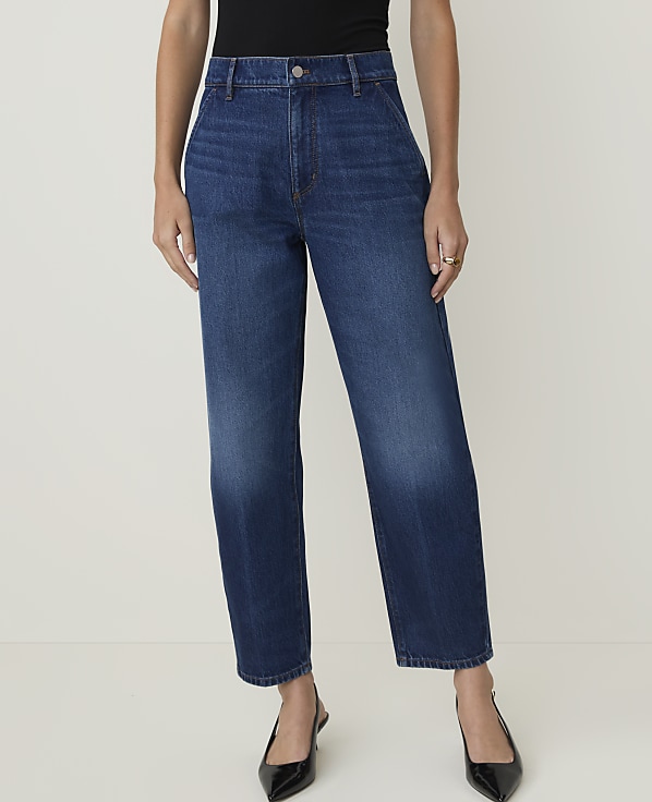 A person stands in dark blue, high-waisted jeans and black heels against a plain white background.