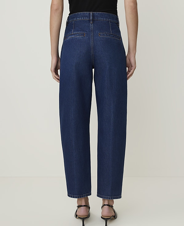 A person wearing dark wash, wide-leg denim jeans stands against a plain, light-colored background.