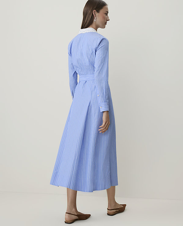 A woman in a blue and white striped dress stands against a plain, light background.