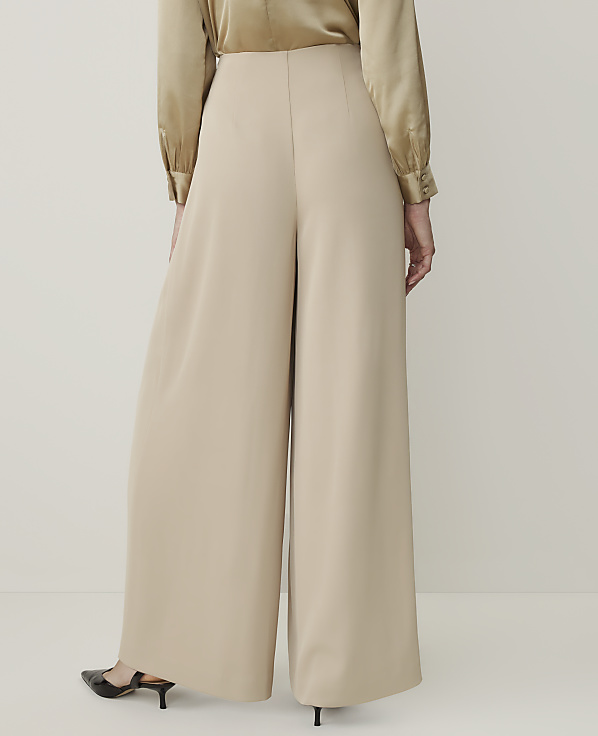 A person wearing beige wide-leg pants and a gold satin blouse stands against a plain white background.