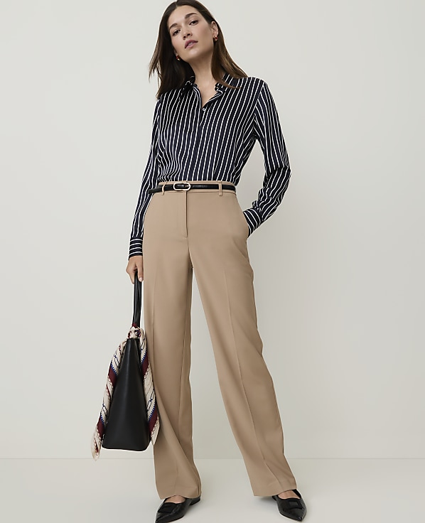 A person wearing light-wash wide-leg jeans and white heeled sandals stands against a plain white background.