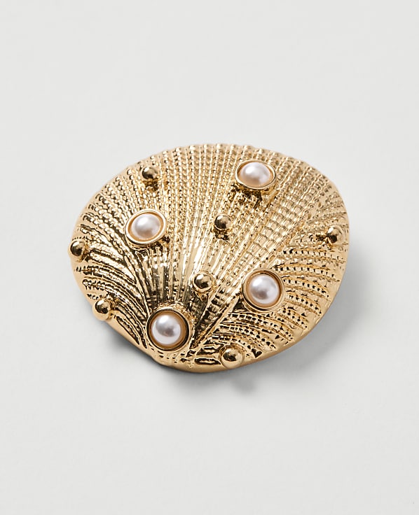 A golden seashell brooch with pearls is set against a plain white background.