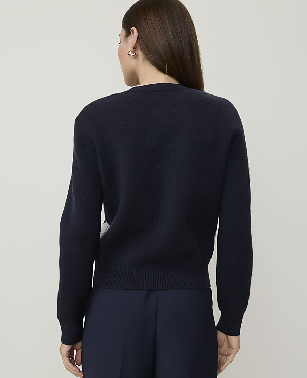 A woman in a dark blue sweater and pants stands against a plain, light gray background.