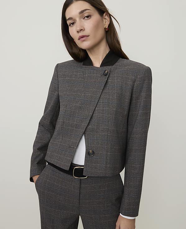 A woman in a plaid jacket and pants stands against a plain, light gray background.