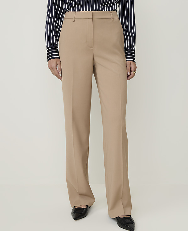A person stands in front of a plain white background, wearing tan trousers, a striped shirt, and black shoes.