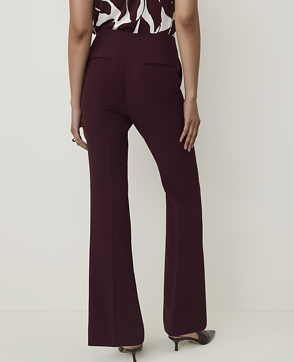 A person wearing burgundy flared trousers and a patterned top stands against a plain white background.