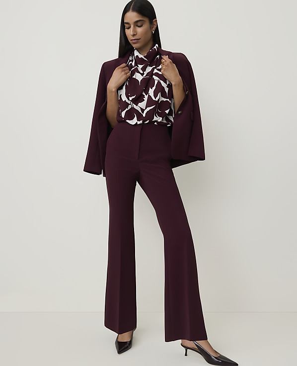 A woman in a burgundy suit with a patterned blouse stands against a plain white background.