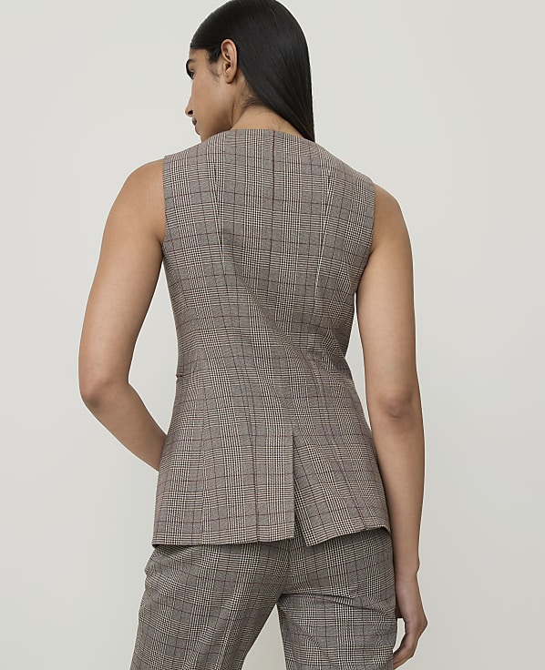A woman in a plaid vest and pants stands against a plain, light-colored background.