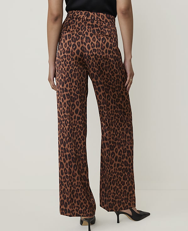 A person wearing leopard print wide-leg pants and black heels stands against a plain, light-colored background.
