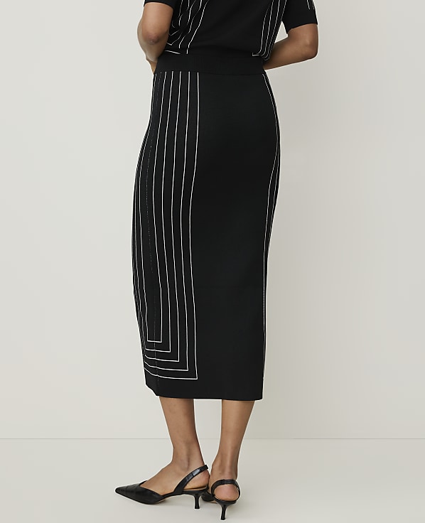 A black midi skirt with white geometric stitching is worn by a person standing against a plain, light-colored background.