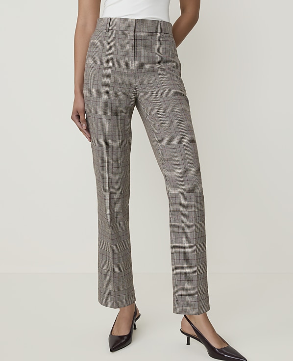 A person stands in the foreground wearing plaid trousers and black heels against a plain, light-colored background.