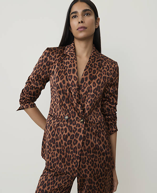 A woman in a leopard print blazer and pants stands against a plain, light-colored background.