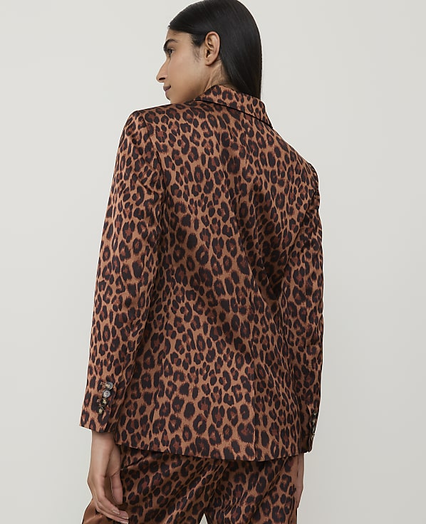 A woman in a leopard-print blazer and pants stands against a plain, light-colored background.