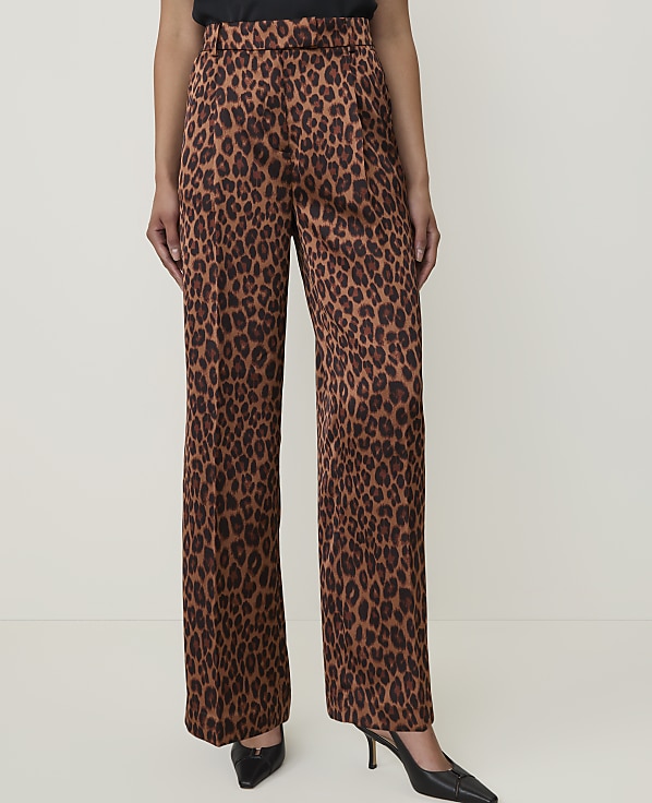 A person stands in the foreground wearing wide-leg leopard print pants and black heels against a plain white background.