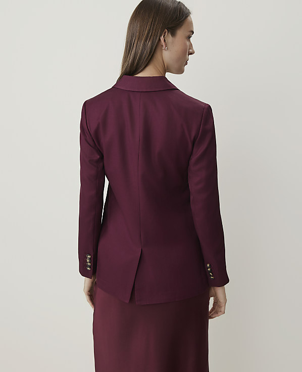 A woman in a burgundy blazer and skirt stands against a plain, light-colored background.