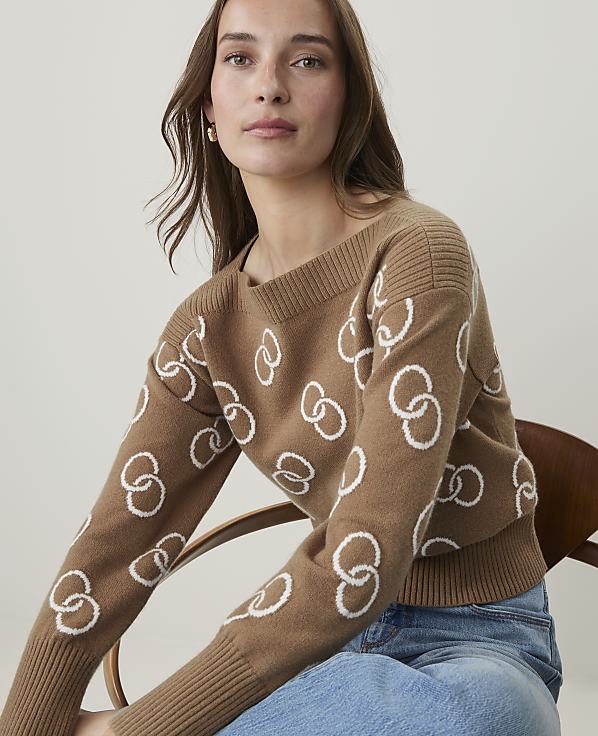 A woman in a brown sweater with a white interlocking ring pattern sits in front of a plain, light-colored background.
