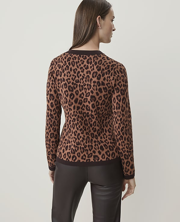 A woman in a leopard print sweater and dark pants stands against a plain, light background.