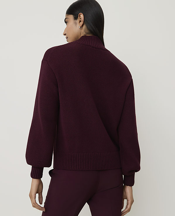 A woman in a burgundy sweater and pants stands against a plain white background.