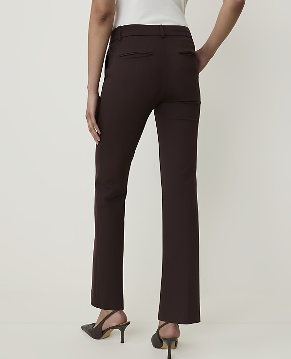 A person wearing brown dress pants and heels stands against a plain, light-colored background.