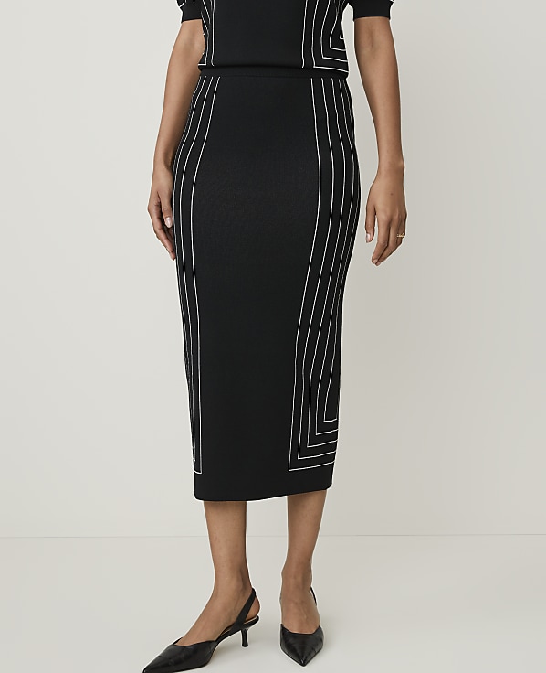 A woman in a black midi skirt with white geometric stitching stands against a plain white background.