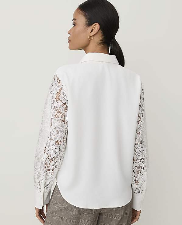 A woman in a white blouse with lace sleeves stands against a plain white background.