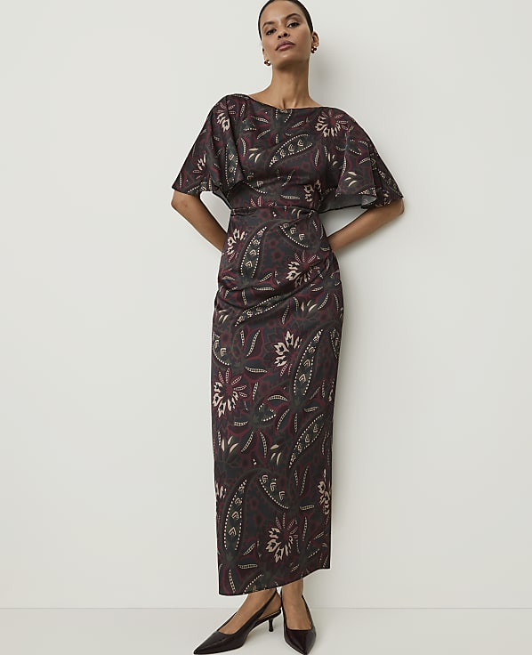 A woman in a patterned dress stands against a plain white background.
