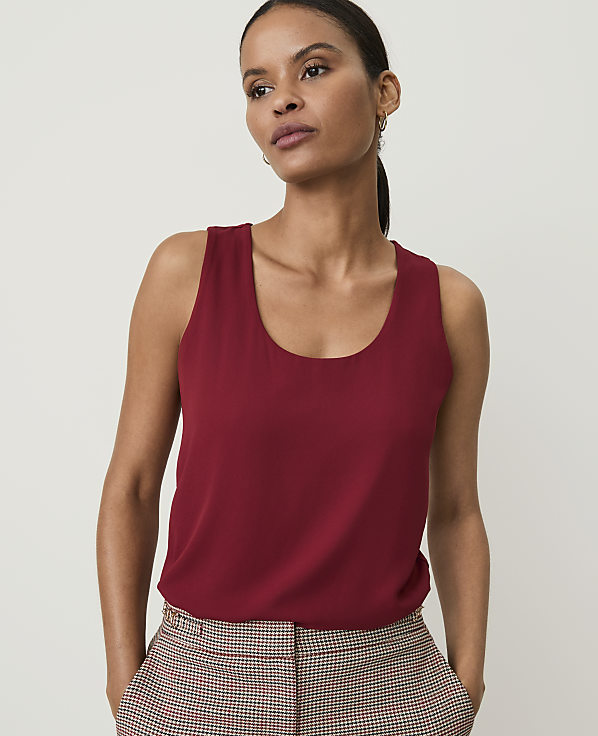 A woman in a red tank top and plaid pants stands against a plain background.