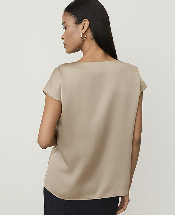 A woman in a tan satin top stands against a plain, light background.