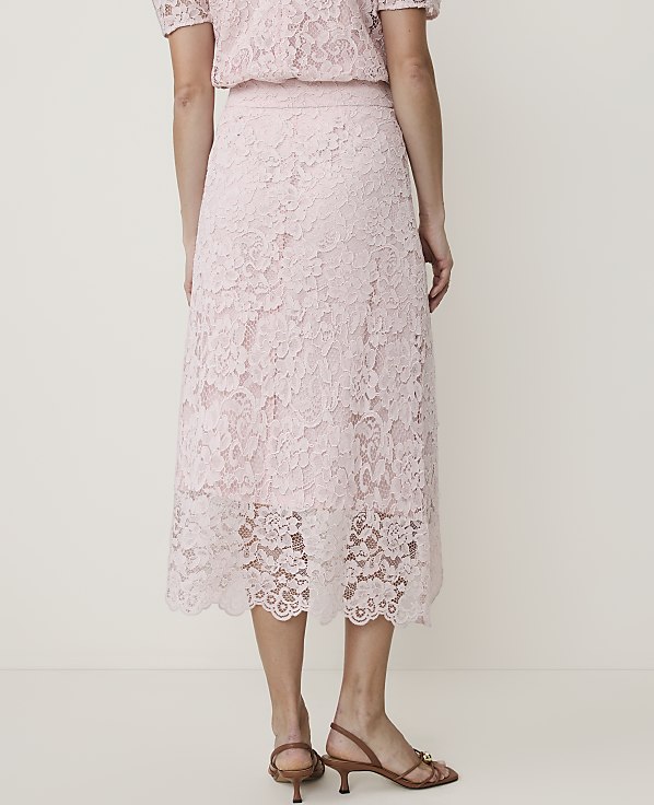 A person stands in a light pink lace skirt and top, with a plain white background.