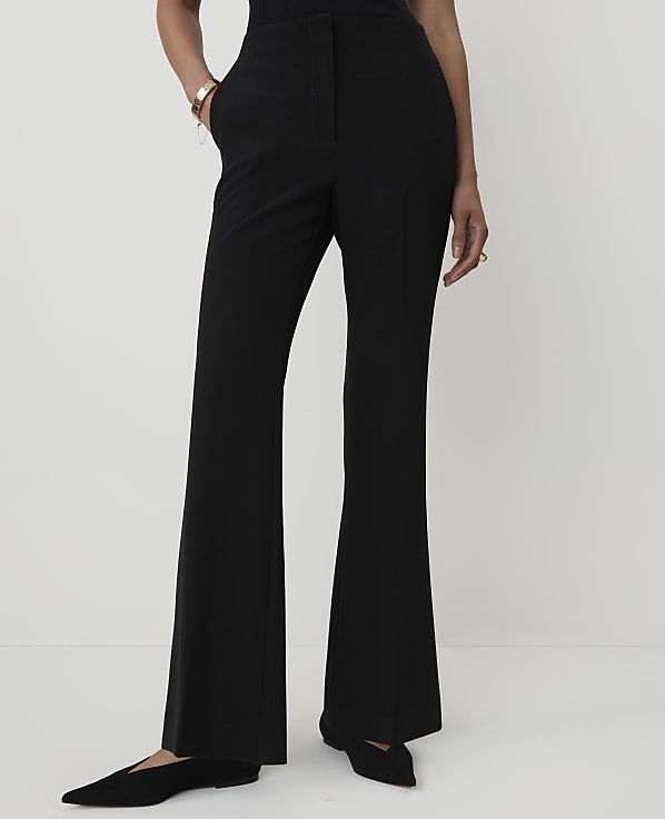 A person wearing black flared pants and pointed-toe flats stands against a plain white background.