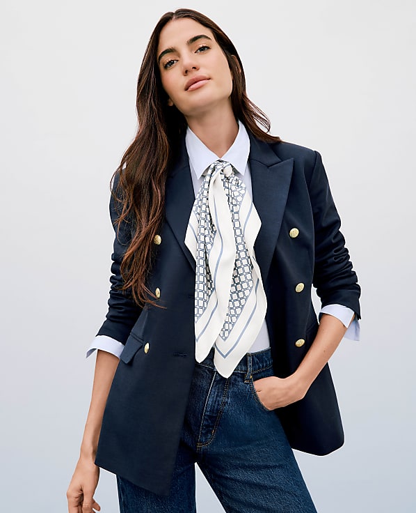 A woman in a navy blazer and jeans stands against a plain white background.