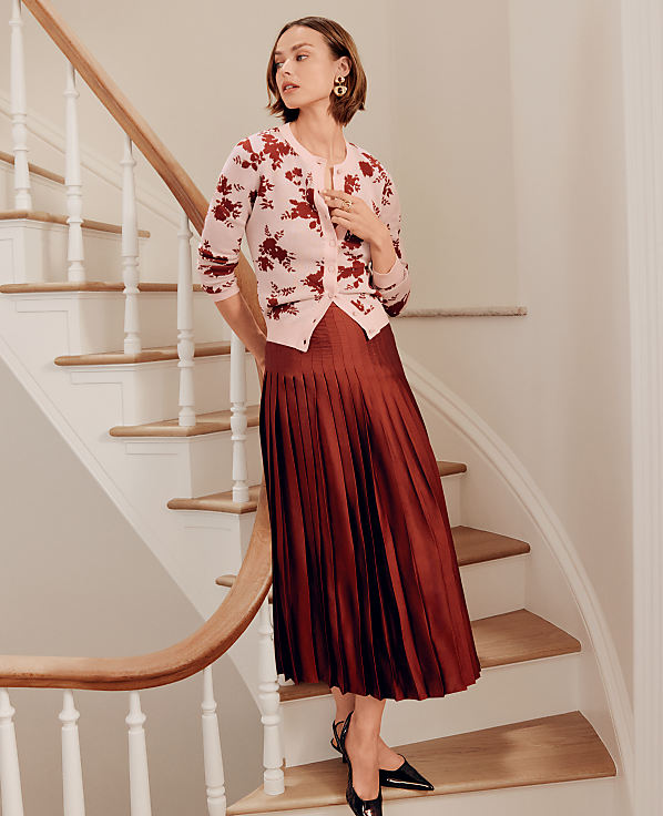 A woman in a floral cardigan and pleated skirt stands on a wooden staircase with a white railing.