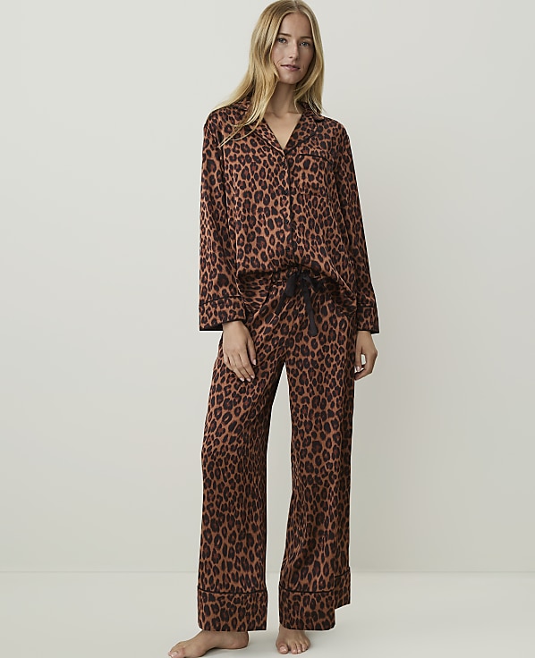 A woman in leopard print pajamas stands against a plain, light-colored background.
