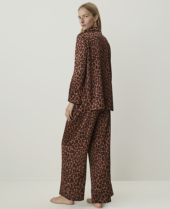 A woman in leopard print pajamas stands against a plain, light brown background.