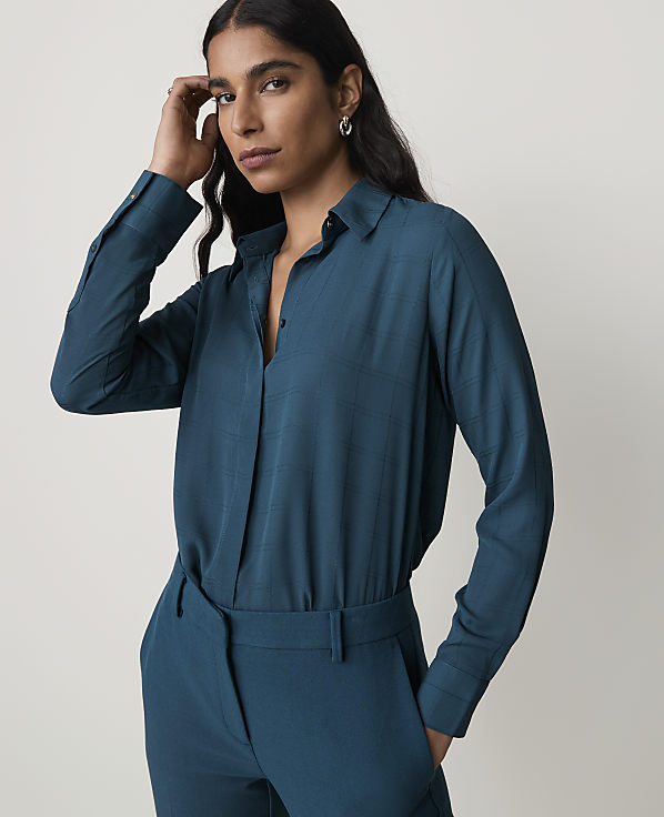 A woman in a teal blouse and matching pants stands against a plain gray background.