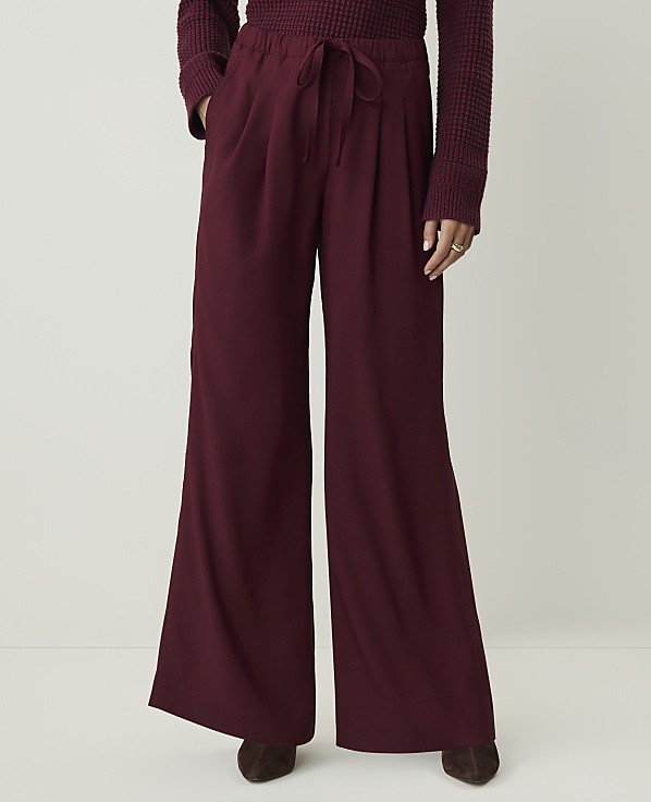 A person stands in maroon wide-leg pants and a maroon sweater against a plain white background.