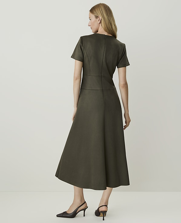 A woman in a dark green dress stands against a plain, light background.