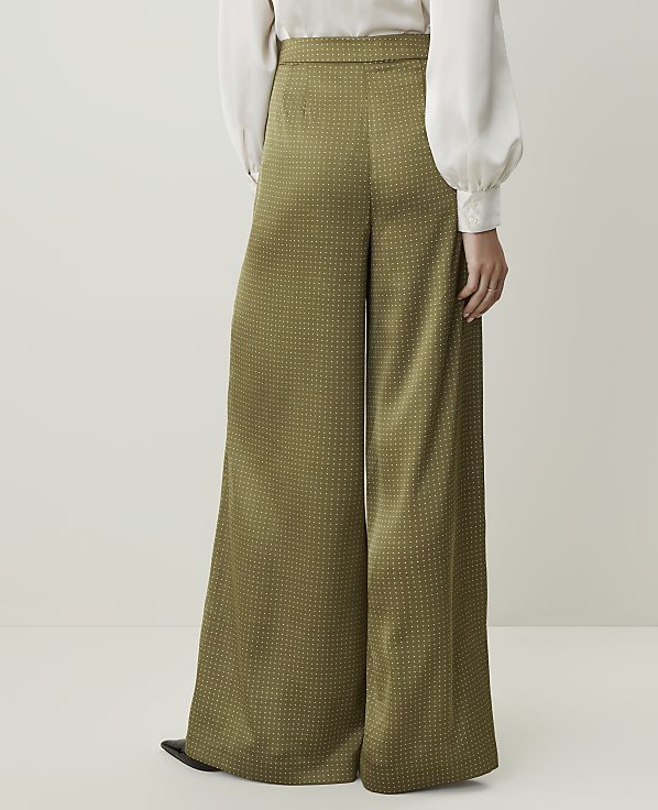 A person wearing wide-leg, olive-green patterned pants stands against a plain, light-colored background.