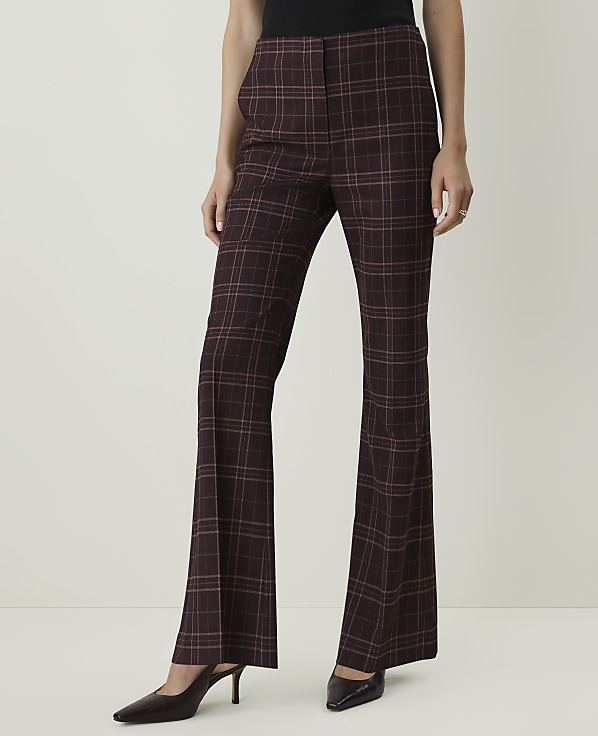 A person wearing maroon plaid flared pants and dark pointed-toe heels stands against a plain white background.
