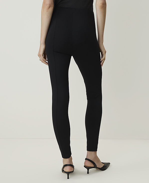 A person wearing black leggings and kitten heels stands against a plain white background.