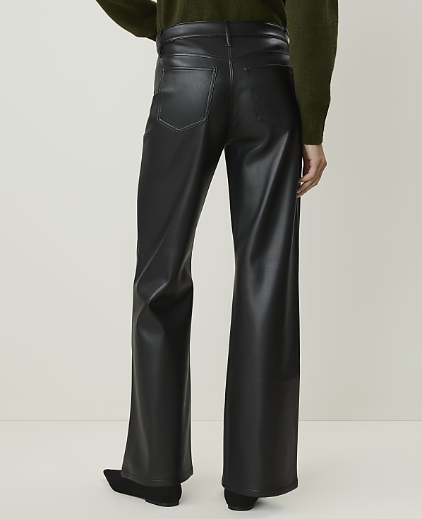 A person wearing black faux leather pants stands against a plain, light-colored background.