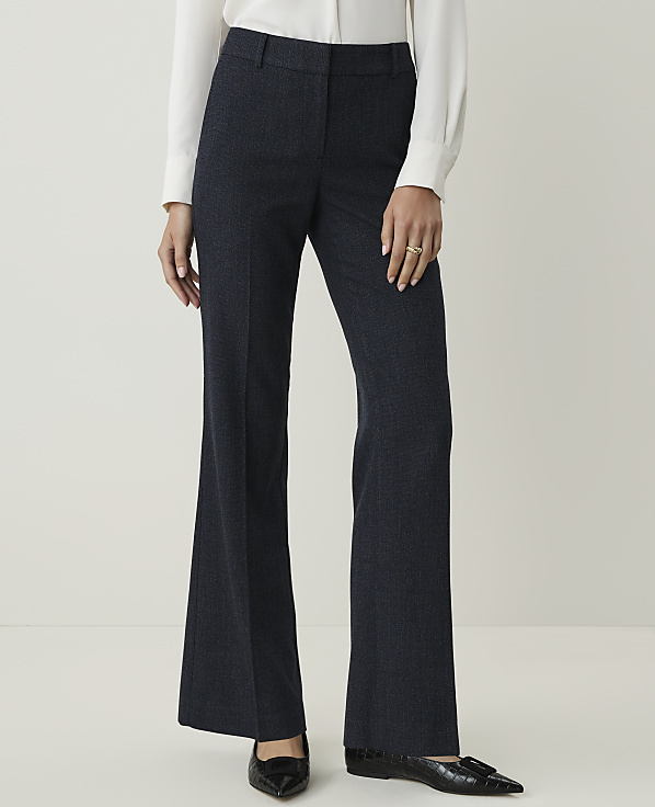 A person in a white blouse and dark patterned pants stands against a plain, light background.