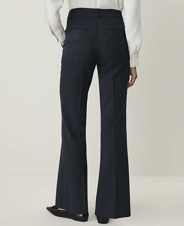 A person wearing dark, flared trousers and a white shirt stands against a plain, light background.