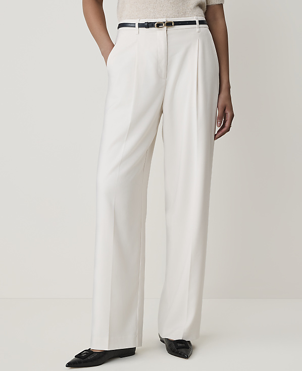 A person stands in cream-colored wide-leg trousers and black flats against a plain white background.